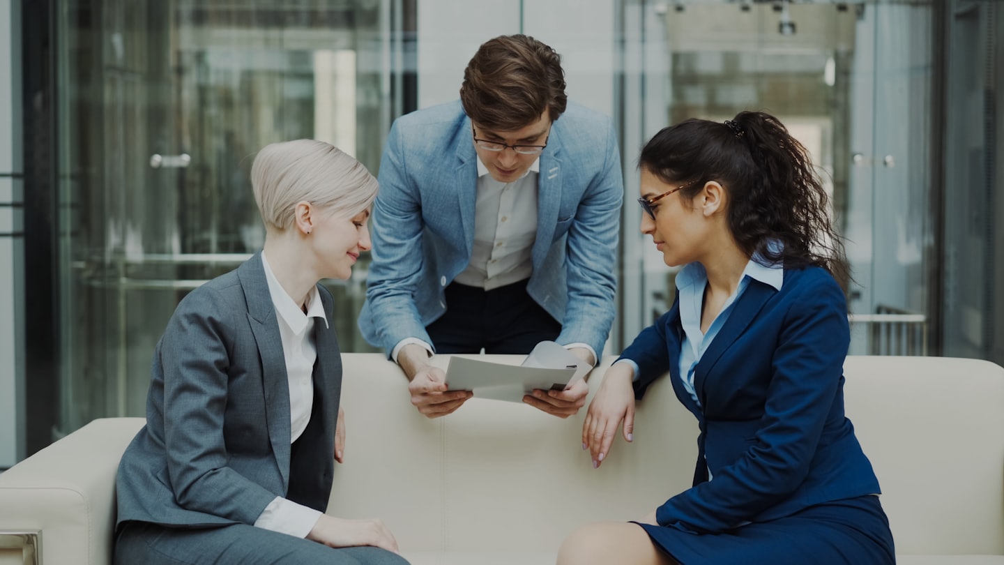 Diverse business team discusses documents on a modern office sofa.